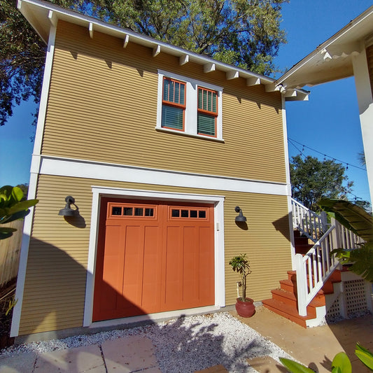 Photo of Shallow Carriage House by Historic Shed. Mustard-colored carriage house with garage door below and exterior steps to apartment above.