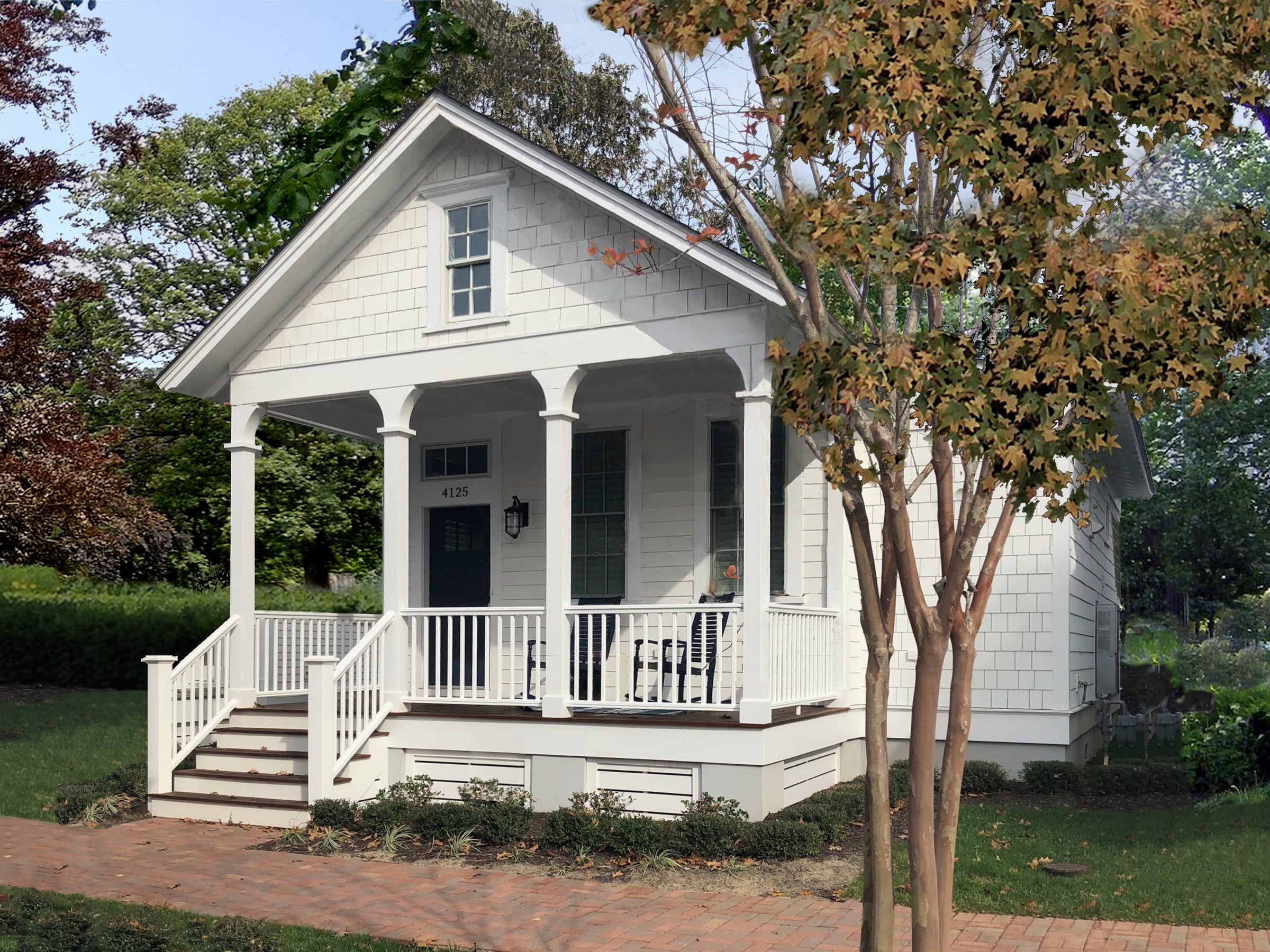 Photo of the Poplar Cove by Jeremy Sommer, a white cottage with a pedimented, three-bay front porch with rocking chair. Surrounded by early autumn landscape.